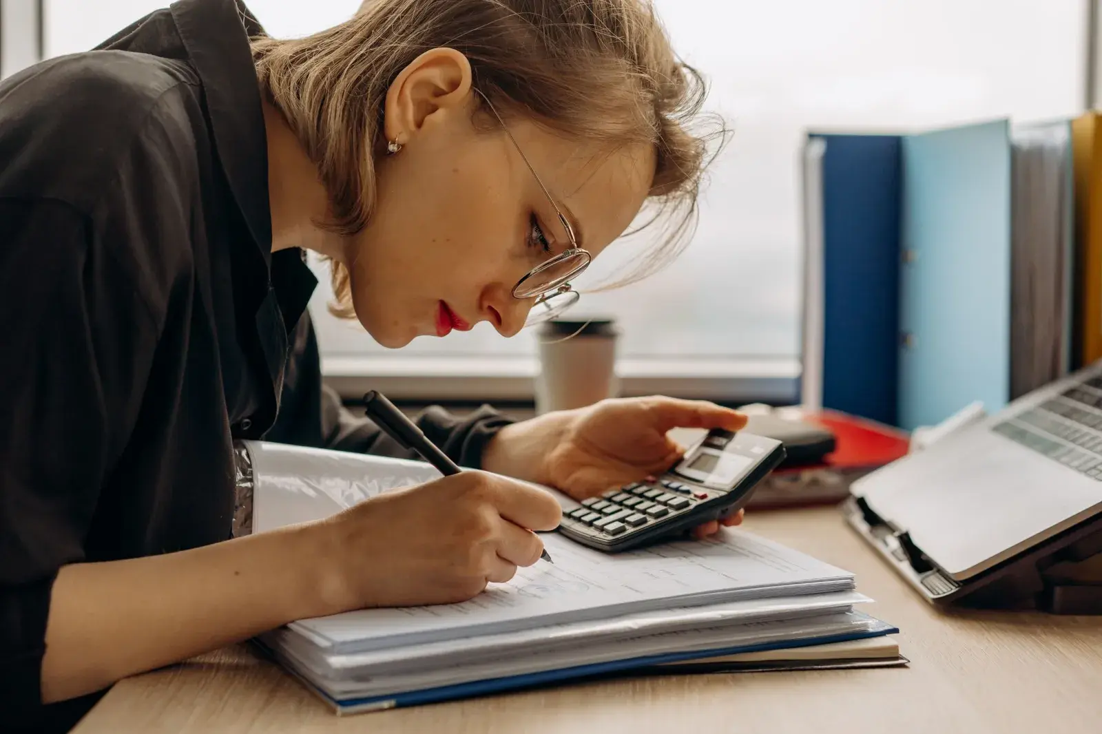 An accountant writing on financial forms while checking figures on a calculator