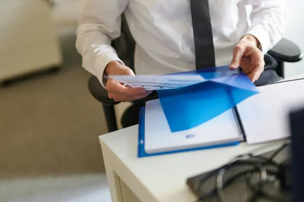 Professional reviewing documents and a blue folder at a desk